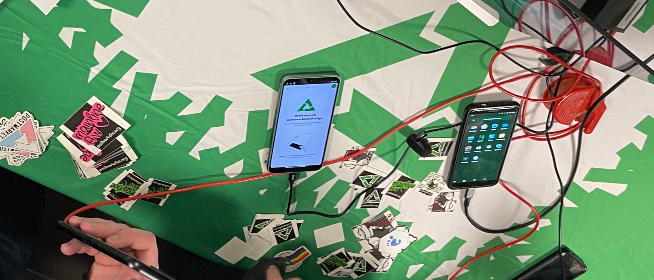 Photo from the FOSDEM table with phones running postmarketOS and stickers